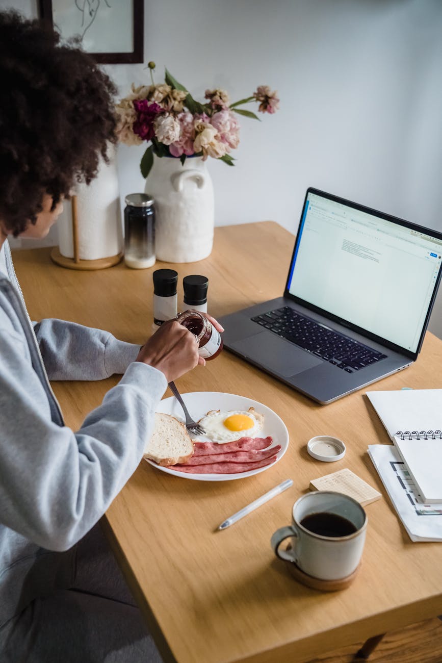 A Woman Eating Breakfast with a Laptop