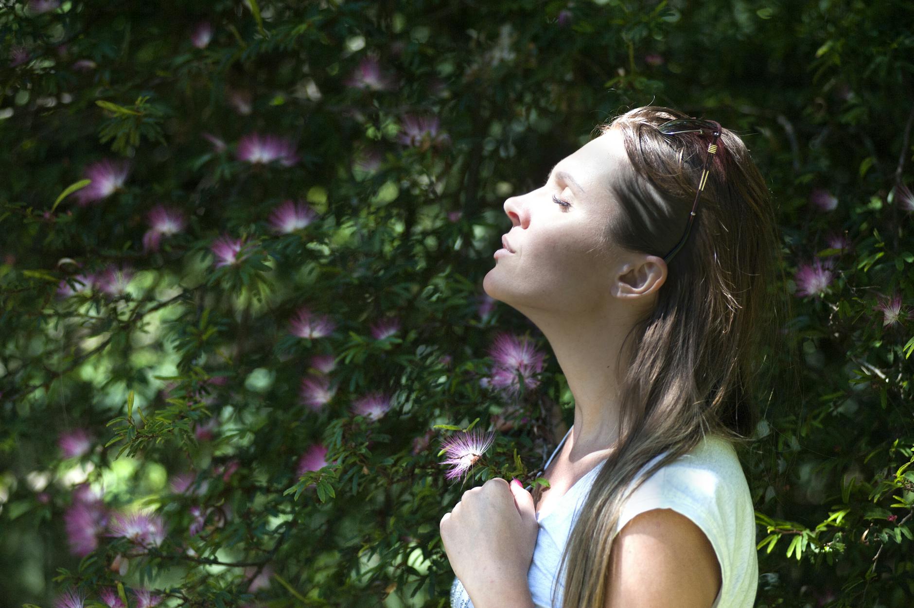 Woman Closing Her Eyes Against Sun Light Standing Near Purple Petaled Flower Plant